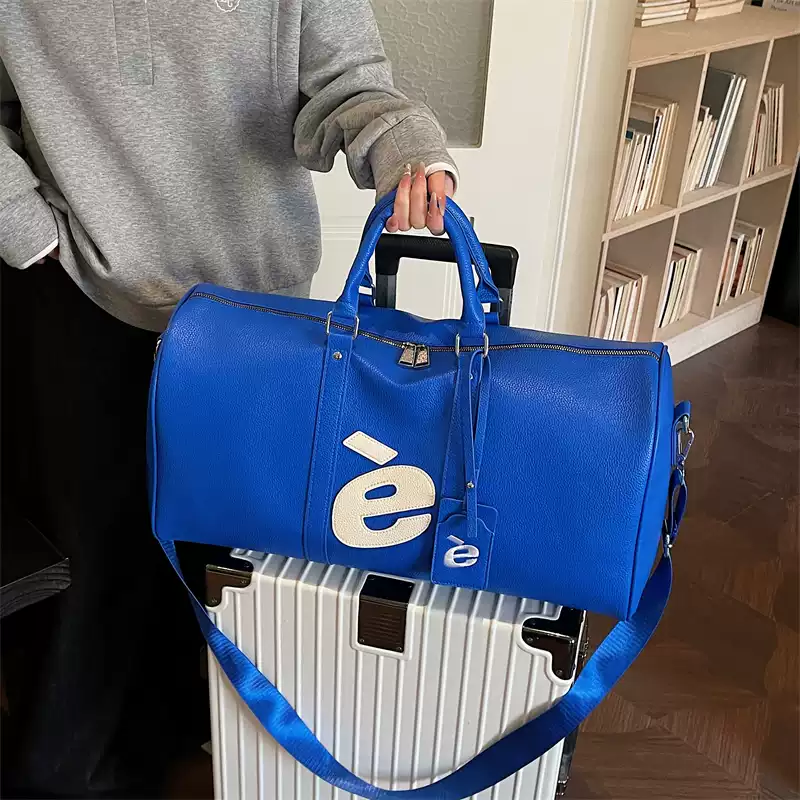 Cobalt blue è Weekender bag carried on top of a rolling suitcase