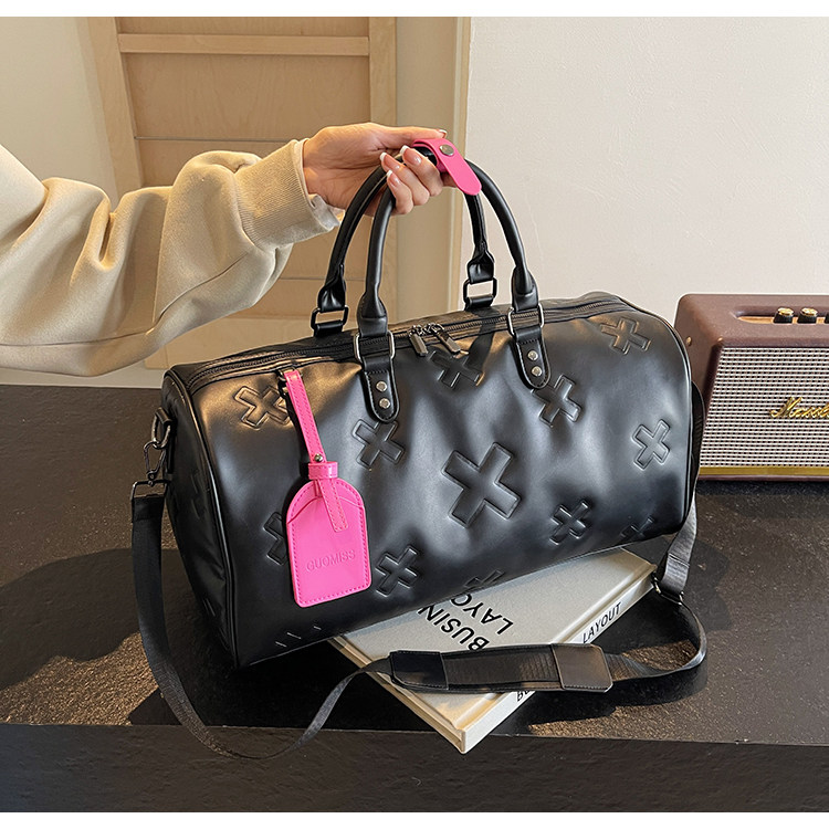 Woman lifting the black è Voyager embossed duffle bag